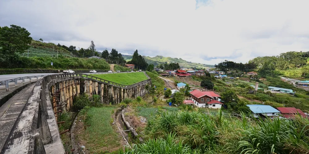 A wide view of Kundasang Valley featuring winding roads, scattered houses, and green highlands.