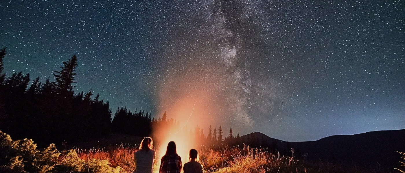 Three sisters sitting by a campfire, stargazing under the night sky in Kundasang.