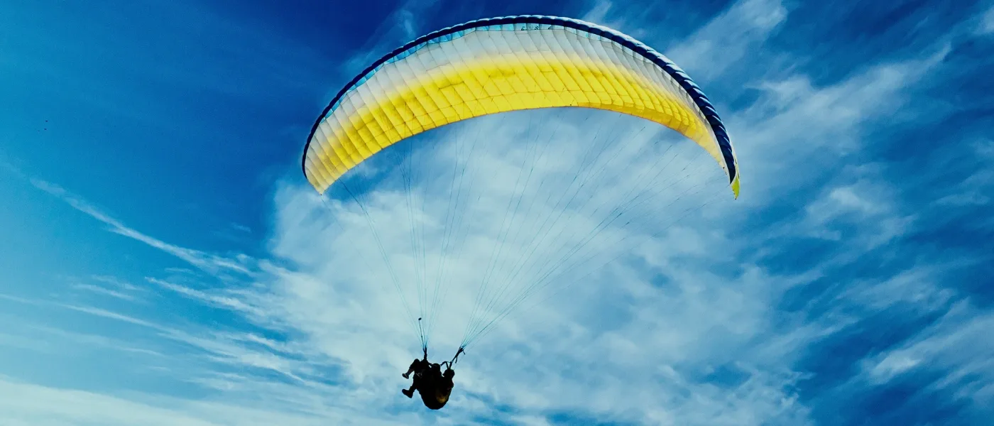 Paraglider flying high above Kundasang captured from below against a clear blue sky.