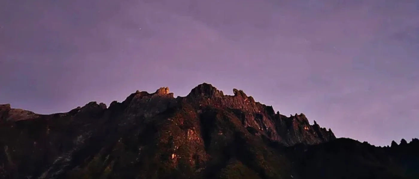 Sunrise view of Mount Kinabalu from Maragang Hill with rocky terrain in the foreground.
