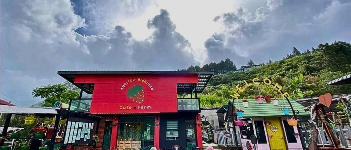 Entrance of Mesilau Highland Strawberry Farm with red house, welcome sign, and surrounding forest and farms.