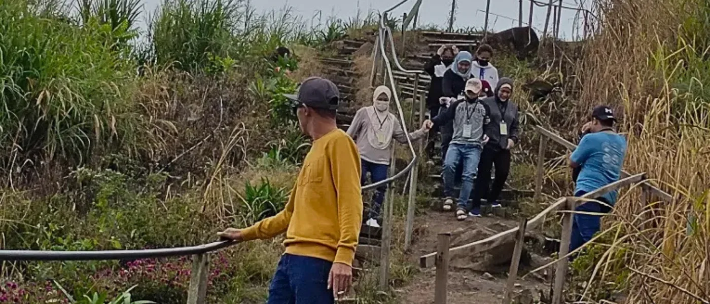 Group of visitors walking down the rustic trail and steps at Sosodikon Hill surrounded by tall grass and greenery
