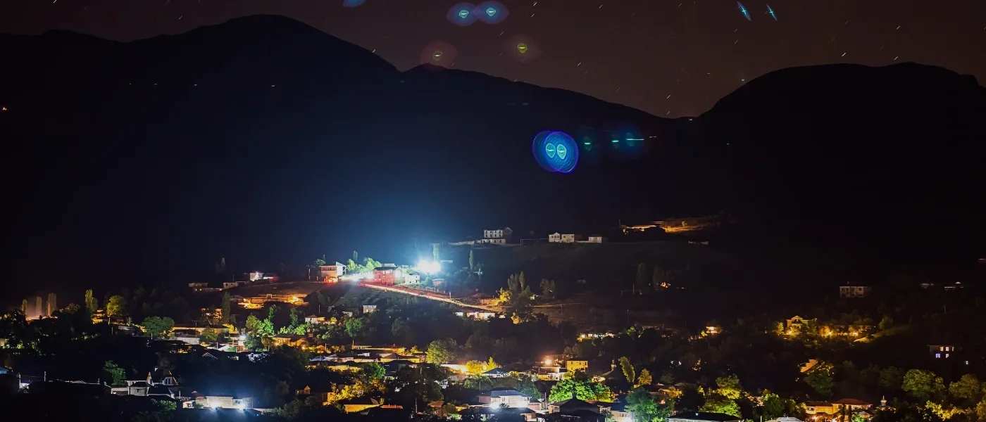 Nighttime view of Kundasang town lights with Mount Kinabalu silhouette in the background, popular stargazing location.